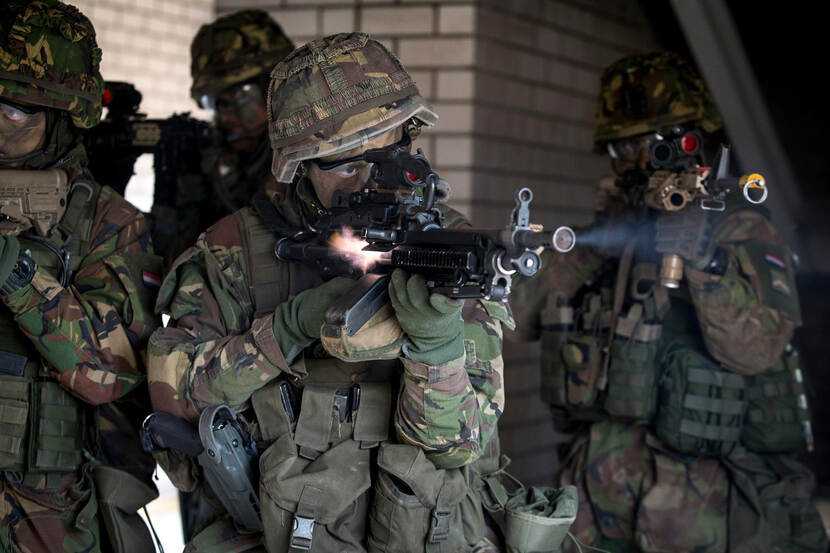 Gecamoufleerde militairen kijken door het vizier van hun wapen. Een van hen vuurt.