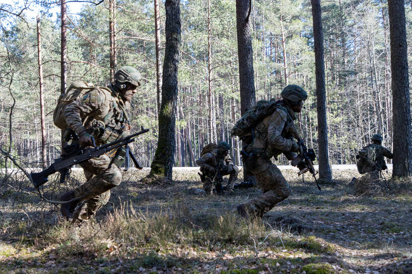 4 militairen in gevechtsuitrusting in actie tussen bomen.