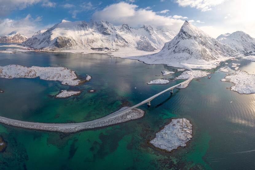 Luchtfoto van wateren tussen besneeuwde ijstoppen, met in het midden een brug.