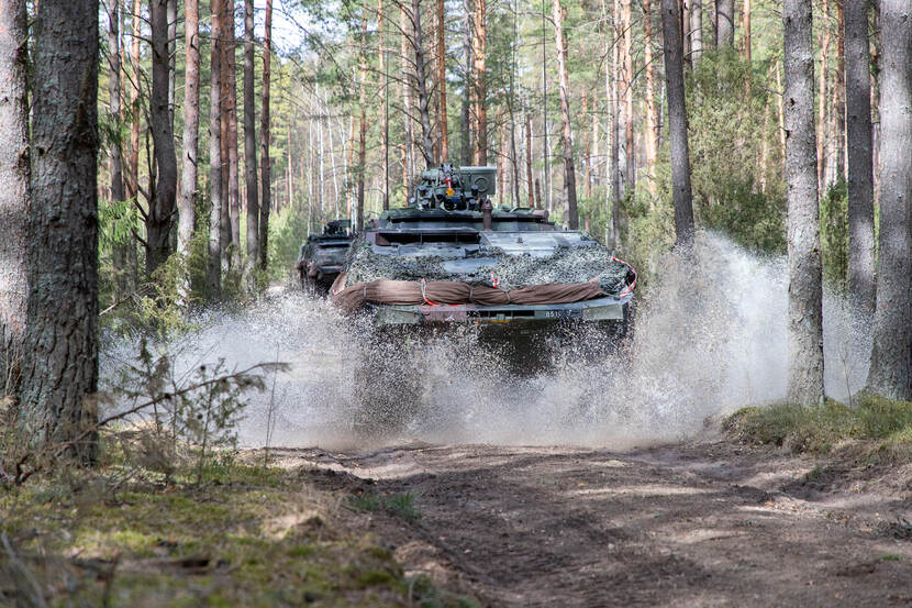 Militair voertuig rijdt door opspattend water in een bos.