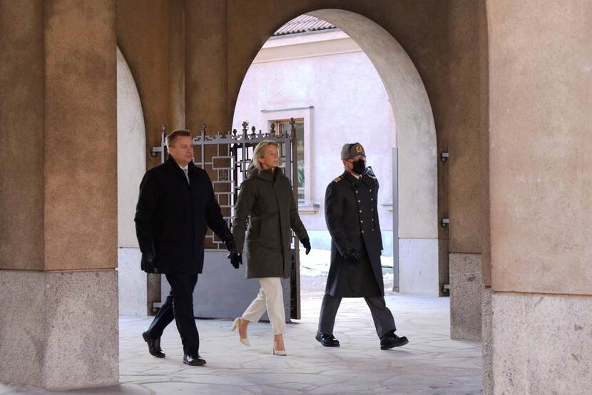 Minister loopt met 2 mannen onder poort door.