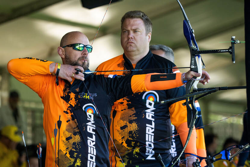 Marco Tessers legt aan voor een schot, terwijl Michel Jansen geconcentreerd kijkt in de aanloop naar zijn beurt bij het boogschieten.