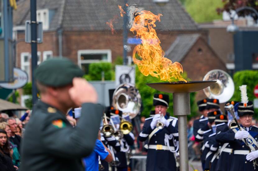 Militair salueert bij het bevrijdingsvuur op het 5 Meiplein in Wageningen. Militair muziekkorps op de achtergrond.