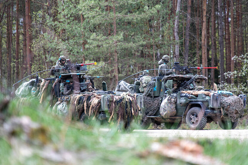 2 gecamoufleerde militaire voertuigen rijden in het bos.
