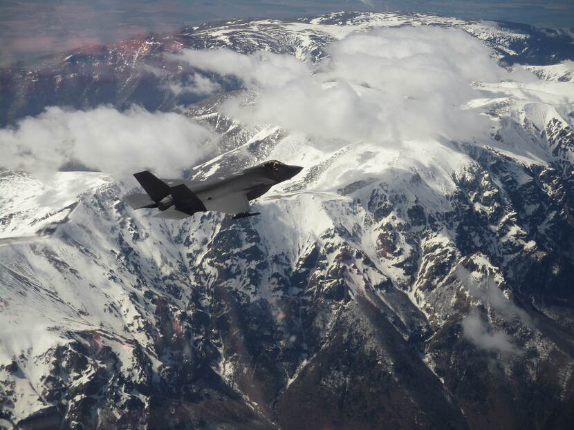 F-35 vliegt tussen wolken boven besneeuwde bergen.