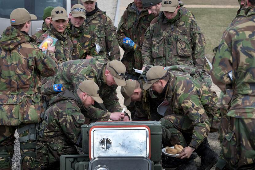 Groep militairen aan het eten in het veld.