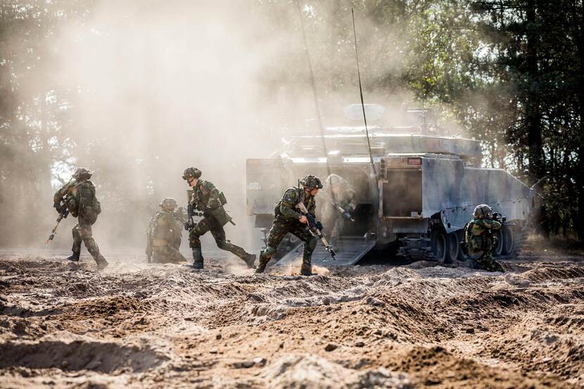 Gewapende militairen rennen uit een tank in het bos.