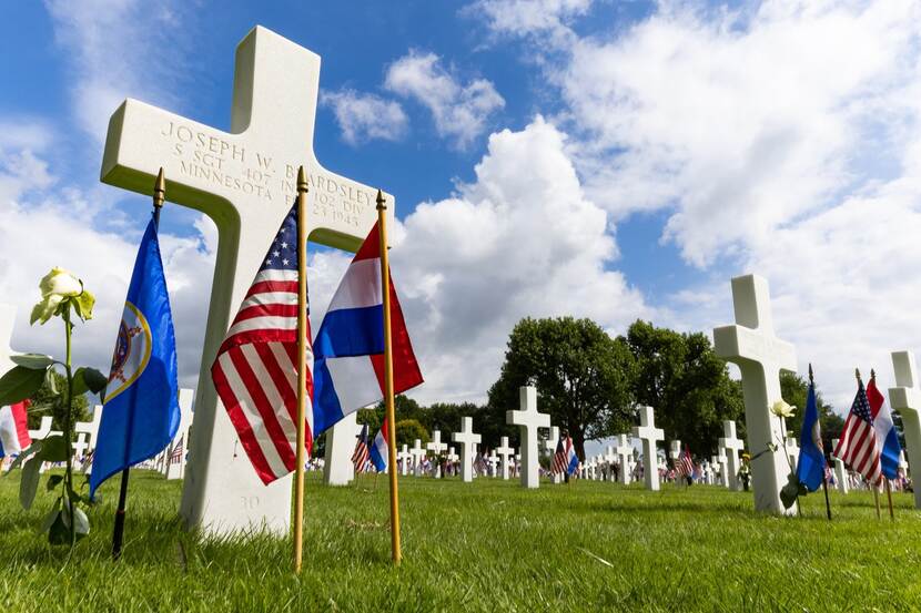 Kruizen met Amerikaanse en Nederlandse vlaggen op begraafplaats.