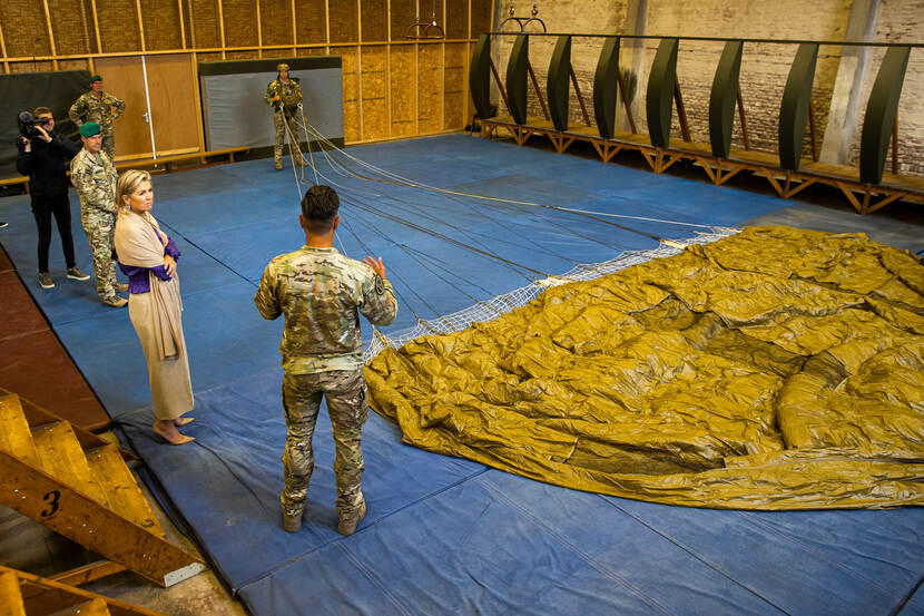 Koningin Maxima krijgt bij de Defensie Para School uitleg over springen met een parachute, deze ligt uitgevouwen op de vloer.