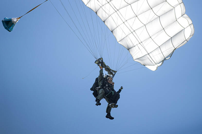 Koningin Maxima hangt met een commando onder een parachute in de lucht.