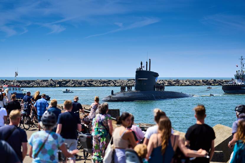 Onderzeeer vaart de haven van Scheveningen in, publiek kijkt toe vanaf de kade.