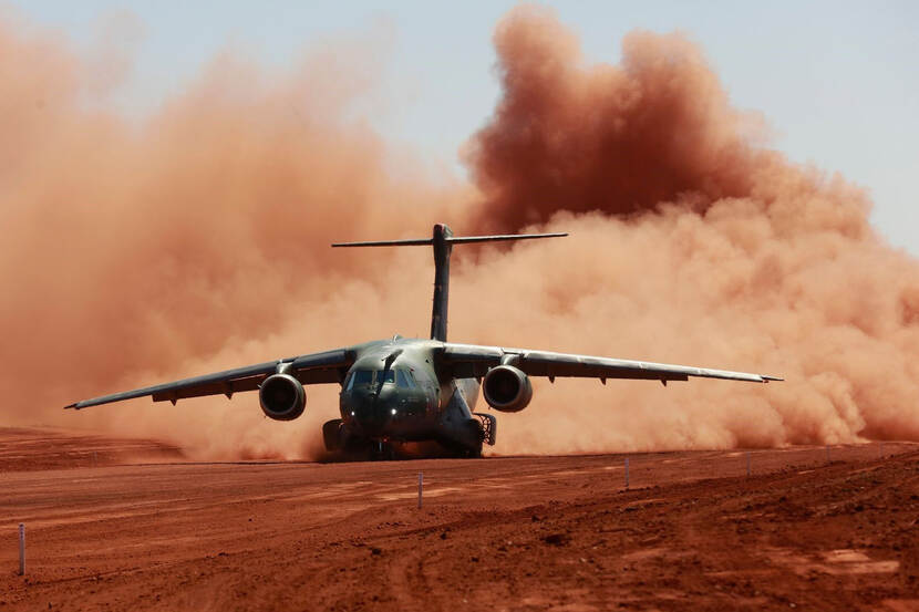 Een C-390M landt op zandgrond, in een grote zandwolk.