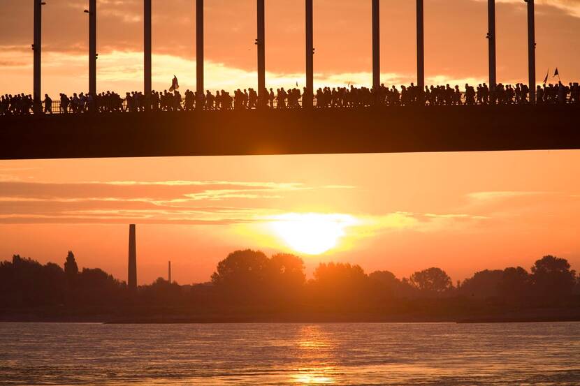 Wandelaars lopen over een brug, de zon komt net op.