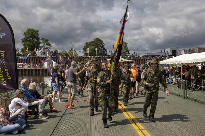 Groep Duitse militairen lopen over een brug tijdens de 4Daagse, een van hen draagt een vlag.
