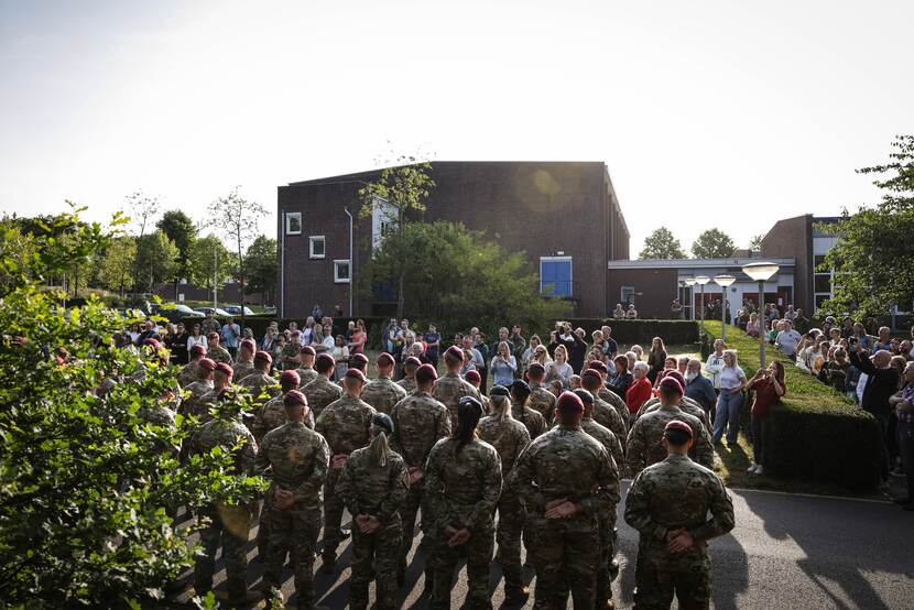 Militairen op hun rug gefotografeerd. Burgers staan voor hen.