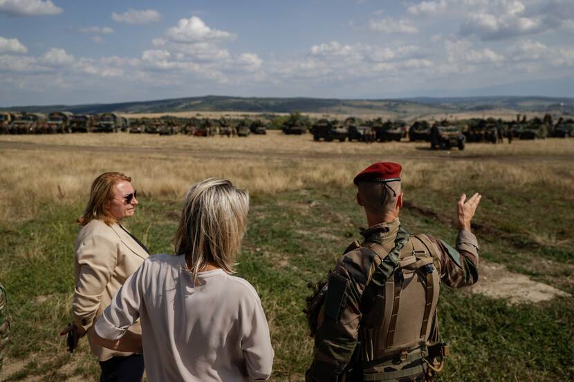 Minister Ollongren in veld bij militairen in Roemenië. Op achtergrond militaire voertuigen.