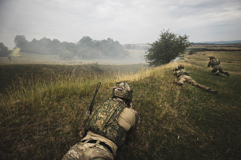 Gewapende militairen liggen op hun buik in Roemeens landschap.