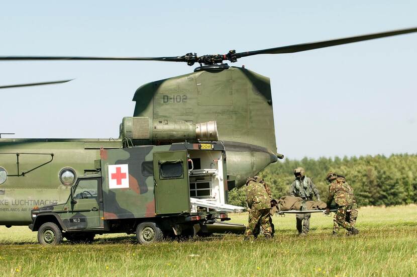 Deel van Chinook-transporthelikopter met militair voertuig voor ziekenvervoer ervoor.