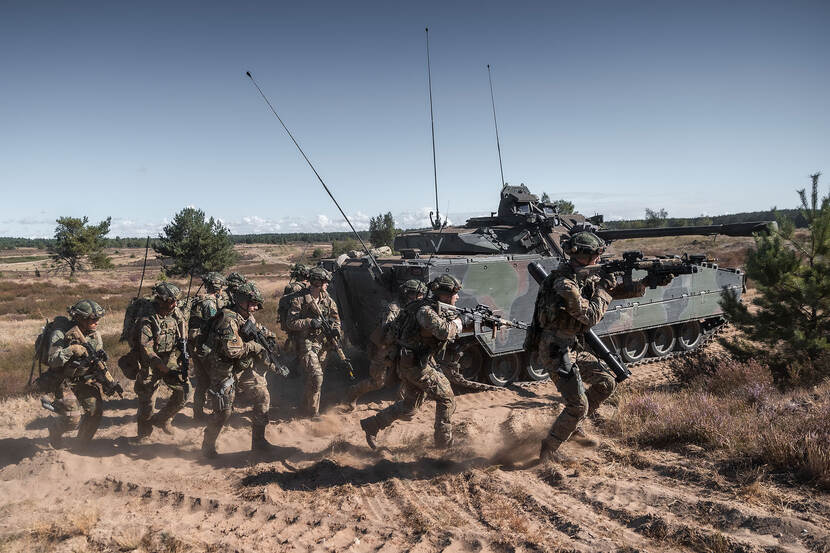 Bewapende militairen en tank in zandgebied.