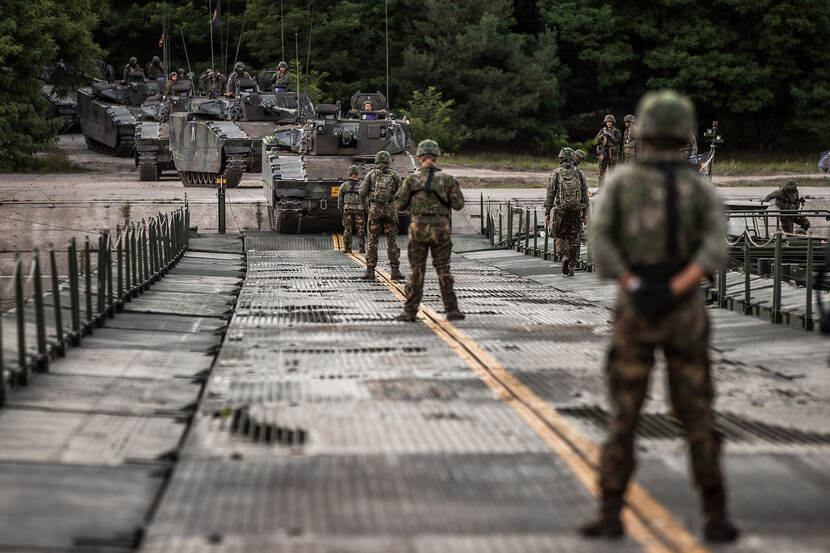 Militairen staan op een noodbrug, tanks naderen om over te steken.
