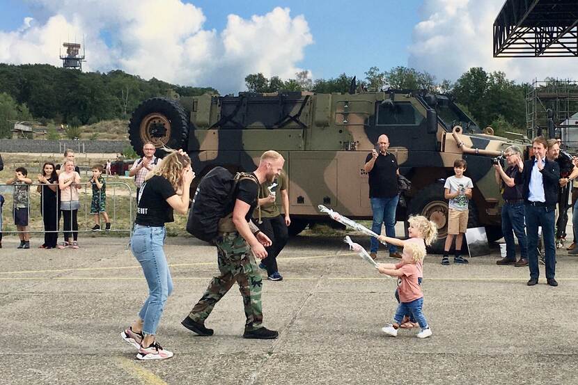 Imthorn wordt begroet vrouw en dochters. Militair voertuig en applaudisserende mensen op de achtergrond.