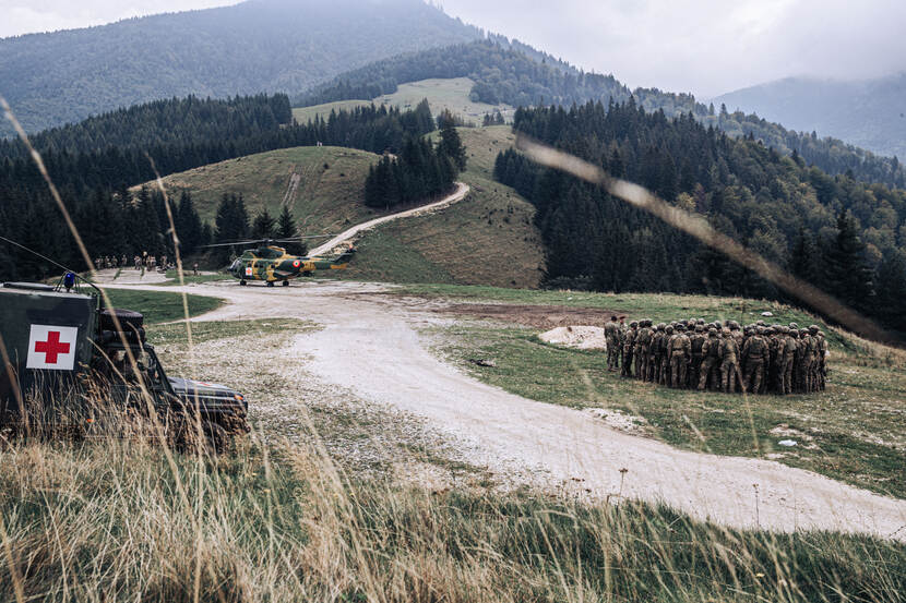Groep militairen, terreinwagen met rood kruis en een Roemeense Puma-helikopter in de Transsylvanische Alpen.
