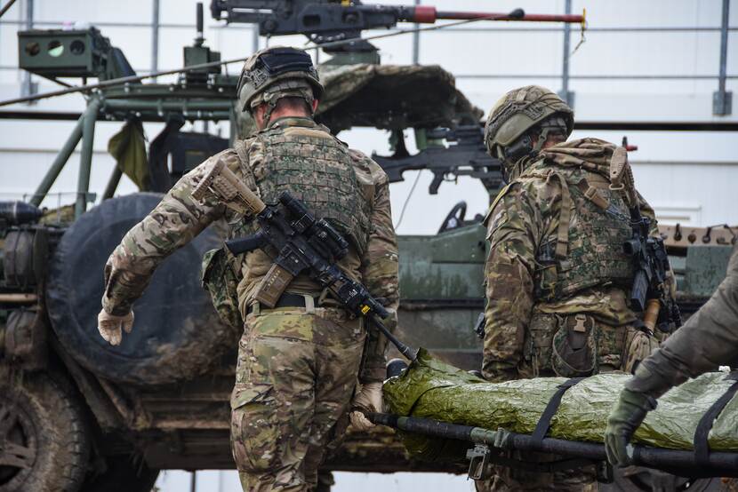 Militairen dragen brancard naar voertuig.