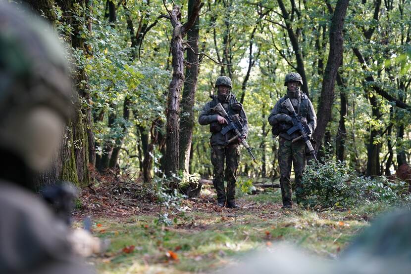 2 militairen met wapen lopen door een bos.