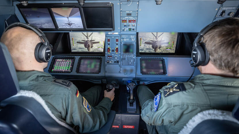 2 militairen kijken op beeldschermen naar het bijtanken van een jachtvliegtuig in de lucht.