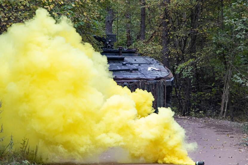 A military vehicle drives through yellow smoke.