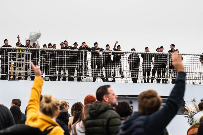 Familie op de kade zwaait naar marinepersoneel aan boord.