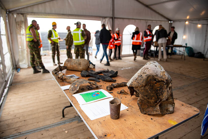 Wrakstukken van een vliegtuig op een tafel. Militairen erbij in gele en oranje hesjes.