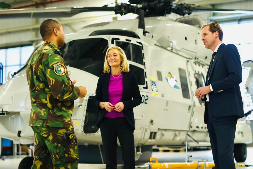 De 2 bewindslieden spreken met een militair, staand voor een helikopter.