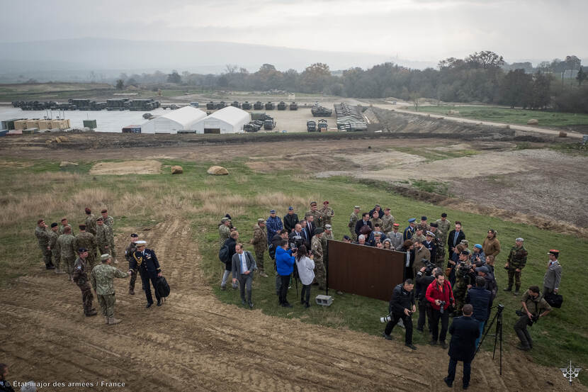 Groep mensen naast een militair kamp, van bovenaf gezien.