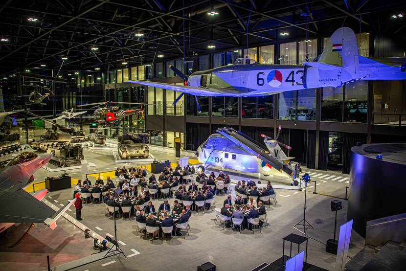 Mensen aan ronde tafels in het Nationaal Militair Museum. Foto van bovenaf genomen.