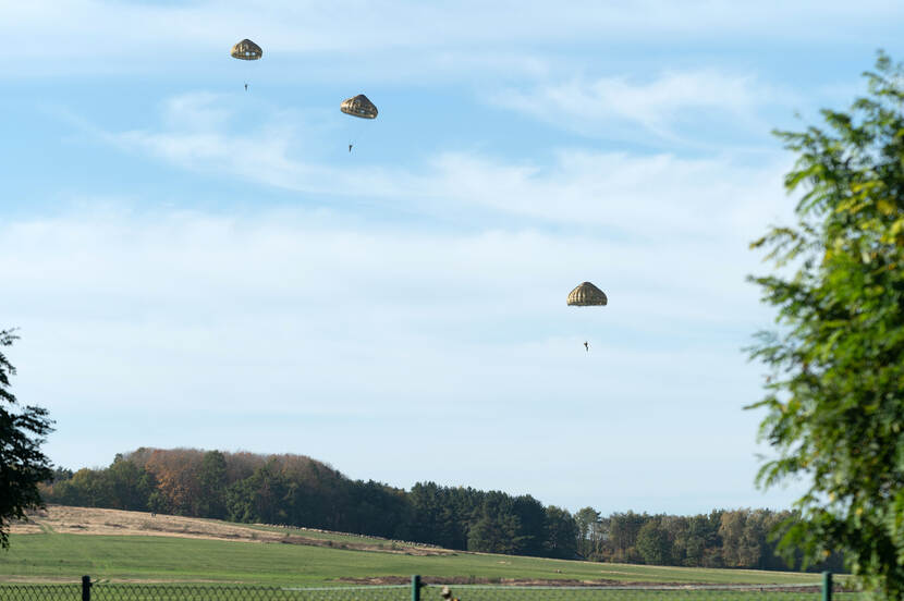 3 militairen zweven boven een groot grasveld aan nieuwe parachutes.