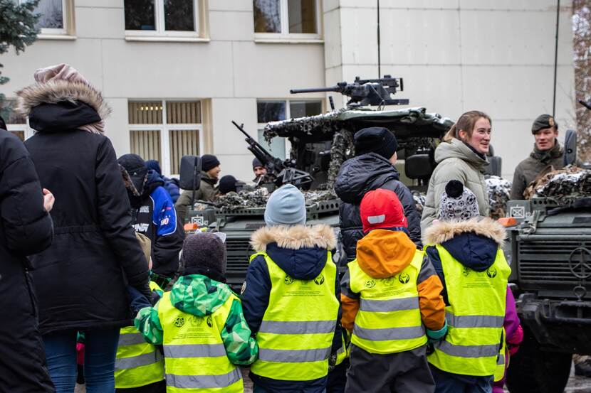 Kinderen (op de rug gezien) kijken bij de militaire voertuigen.