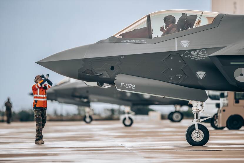 Neus van F-35 met vlieger in cockpit op de grond. Man in oranje pak geeft aanwijzing.