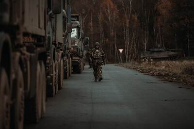 Militair loopt tussen transportvoertuigen en gevechtsvoertuig.