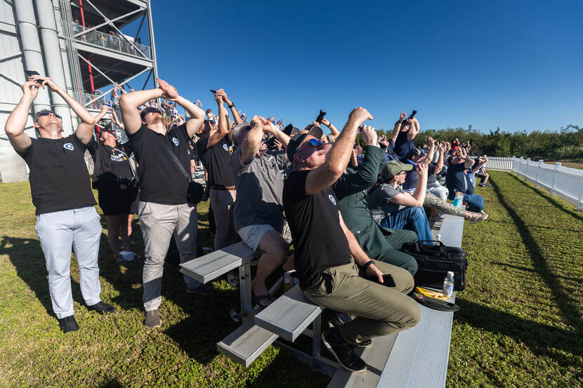 Vele toeschouwers met een zonnebril op filmen met hun telefoon de lancering van de raket.