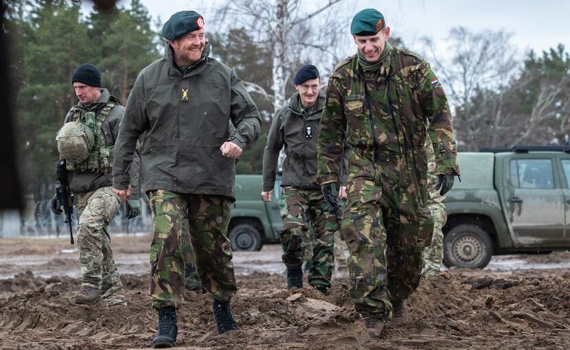 Koning in landmachtuniform loopt naast militair.