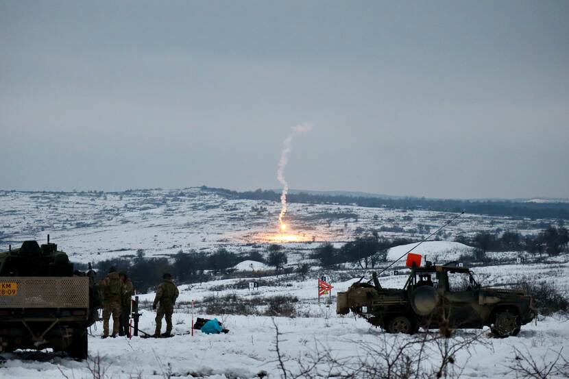 Lichtgranaat komt neer in besneeuwd landschap. Op de voorgrond militaire voertuigen.