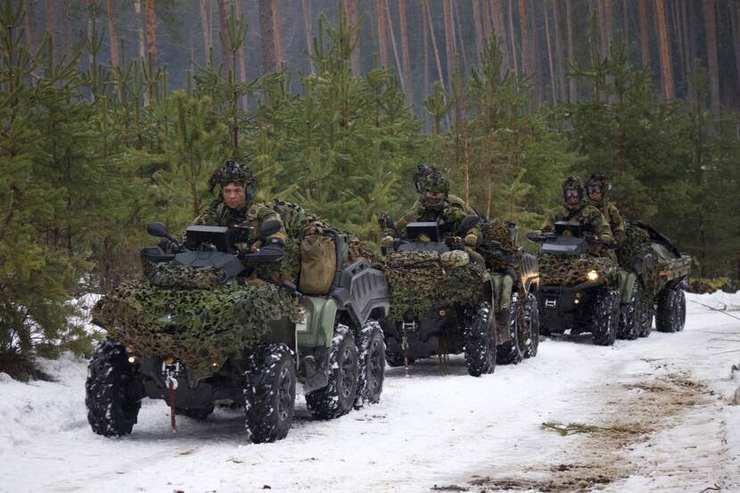 3 militaire voertuigen rijden achter elkaar in de sneeuw in het bos.