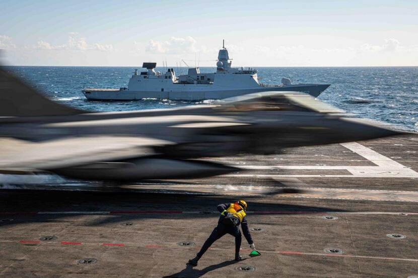 Vliegtuig stijgt op van vliegdekschip. Zr.Ms. De Zeven Provincien ligt langszij.