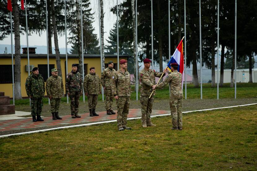 Militairen dragen met Nederlandse vlag het commando over. Op de achtergrond rijtje buitenlandse militairen.