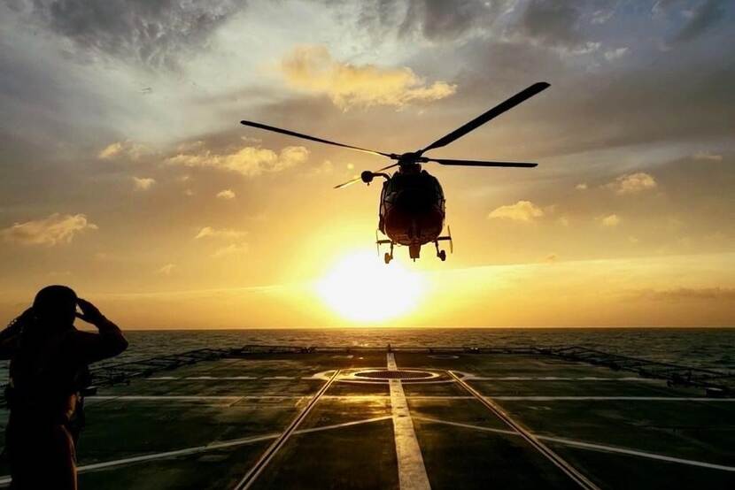 Helikopter landt op dek schip tijdens ondergaande zon.