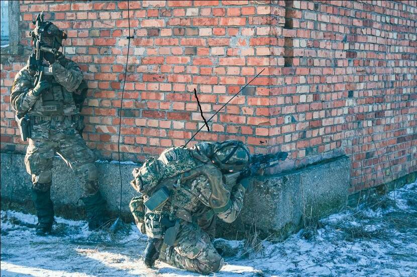 Gewapende militairen staan achter een huis.