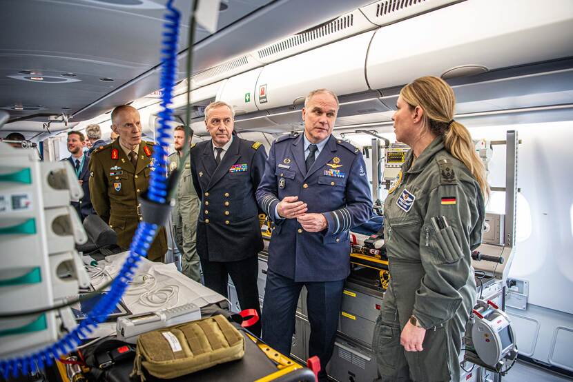 Commandant der Strijdkrachten en zijn buitenlandse collega's in gesprek met vrouwelijke militair in een vliegtuig.