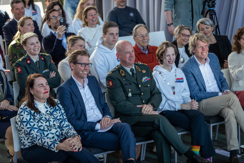 De staatssecretaris en commandant landstrijdkrachten in het publiek bij een herdenking.