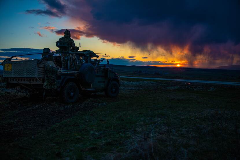 Avondfoto van een militair op militair voertuig tegen een ondergaande zon.